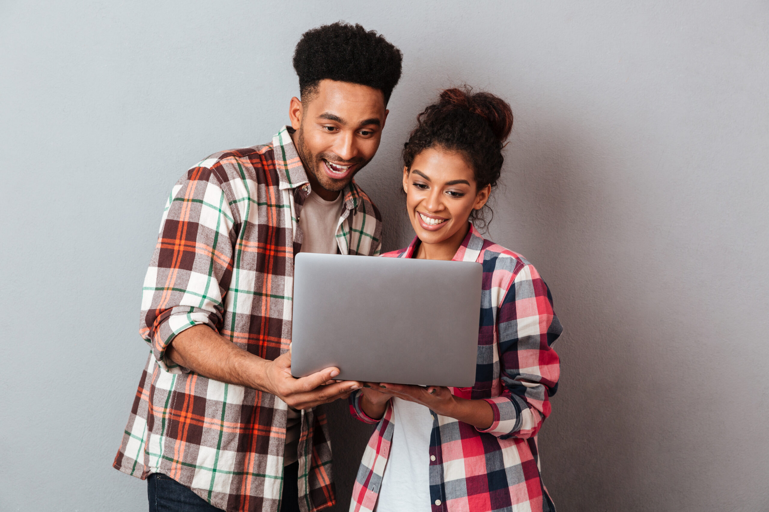 Portrait of a happy young african couple using laptop computer while standing together isolated over gray background